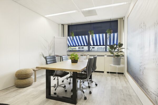 Modern ingerichte vergaderruimte aan de Markerkant 13 met houten tafel, zwarte stoelen, planten en een flip-over met "welkom" erop.